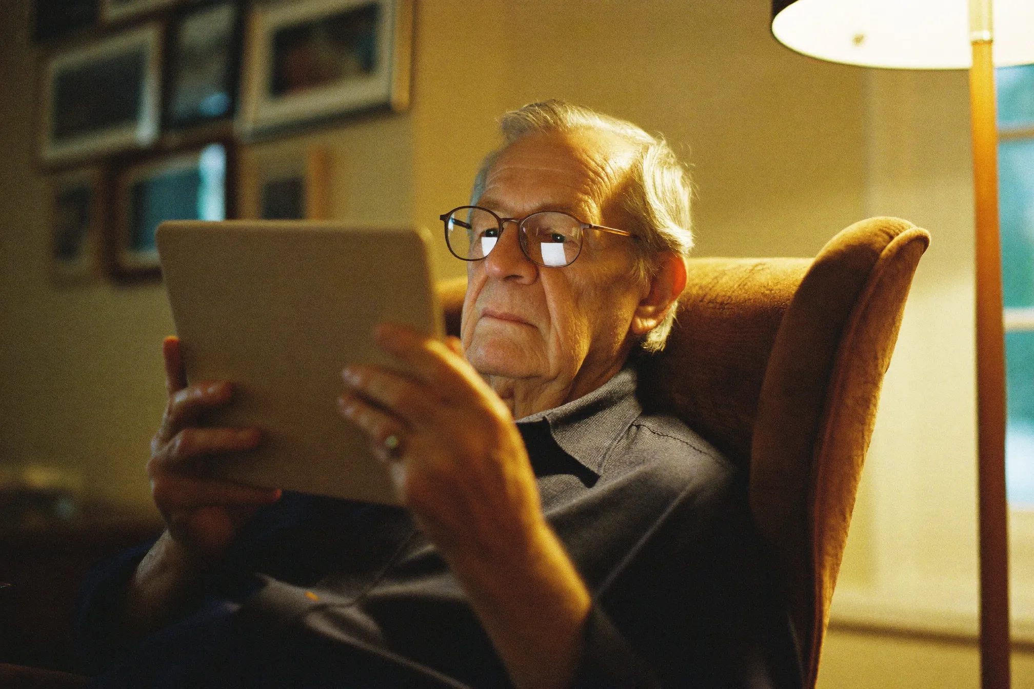 Muž po sedmdesátce si v křesle prohlíží svou kroniku na tabletu